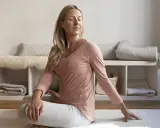 Kvinna i rosa tröja och grå byxor gör en vridning i sittande ställning, en form av gående meditation.