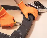 Manos con guantes naranjas usando una grapadora para tapizar una silla.