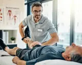 Fizjoterapeuta ćwiczy nogę starszego pacjenta. Rehabilitacja jest kluczowa, by dowiedzieć się, komu przysługuje szpital uzdrowiskowy.