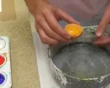 Manos vierten una yema de huevo en un recipiente para preparar una pintura al temple. Paleta con pigmentos de colores al lado.