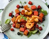 Saftige argentinische Rotgarnelen mit Wassermelonenwürfeln, Tomaten und Basilikum auf einem Teller.