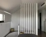 Modern interior with a white slatted partition, possibly to tirar tabique para unir dos pisos. Baskets and a window are visible.