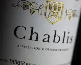 Nahaufnahme eines Etiketts mit der Aufschrift "Chablis". Ein goldenes Wappen mit Trauben und Waage ziert das Etikett dieses Chablis Weins.