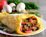Złocisty omlet z pomidorami i pieczarkami, udekorowany koperkiem. Pyszne śniadanie na drewnianym blacie.
