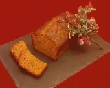 Un délicieux pain d'épice, décoré de baies rouges et de branches givrées, est prêt à être dégusté. Une tranche est déjà coupée.