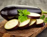 Berenjena entera y rodajas listas para hacer un delicioso puré de berenjena bebé, adornadas con perejil fresco sobre tabla de madera.