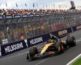 Un coche de Fórmula 1 naranja y negro acelera en Melbourne. Los aficionados vitorean. ¡Qué ganas de que empiece la Fórmula 1 2026!