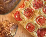 Focaccia receta con tomates frescos y hierbas, junto a un pan rústico y un bollo con almendras.