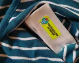 Namensetiketten Kita Erfahrungen: Ein gestreiftes Shirt mit einem gelben Aufkleber "Runzelfüßchen Zschocher" und einem Hausmotiv.