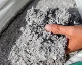 Gros plan sur une main tenant un tas de fibre de cellulose isolant, un matériau gris et vaporeux.