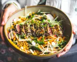 Un délicieux tataki de thon, enrobé de sésame noir et blanc, repose sur un lit de légumes croquants : haricots verts, carottes râpées, radis et champignons enoki.