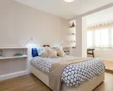 Habitación moderna con cama, estanterías y una apertura que permite tirar tabique para unir dos habitaciones.