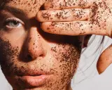 Visage couvert de grains d'un exfoliant chimique naturel, une main cache un œil.