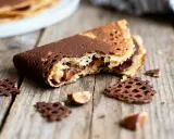 Crêpe dentelle au croustillant praliné, garnie de chocolat et noisettes, sur fond de bois.