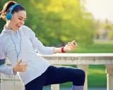 Frau mit Kopfhörern und Handy-Armband spielt Luftgitarre beim Laufen. Perfekte Musik zum Laufen!