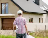 Inżynier w kasku z planami w ręku analizuje kosztorys inwestorski budowy domu.