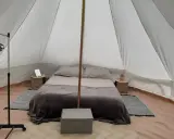 Komfortowy glamping nad morzem: łóżko z pościelą, stoliki nocne, wieszak i namiot.