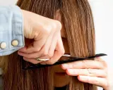 Eine Person schneidet sich mit Kamm und Schere die Haare, um Curtain Bangs zu kreieren.