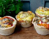 Vier köstliche Mini-Quiches mit verschiedenen Füllungen, perfekt für ein schnelles mini quiche rezept. Mit Petersilie garniert.