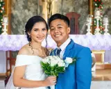 Novios sonriendo, ella con vestido blanco y él con traje azul. Un ramo de rosas blancas. Agradecimiento a los novios por la boda.