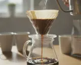 Heißes Wasser fließt langsam durch den Filter, um den perfekten pour over kaffee zuzubereiten. Dampf steigt auf, während der Kaffee in die Kanne tropft.