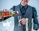 Barman nalewa Olmeca Tequila Gold do miarki, idealna tequila do margarity. Obok kieliszek z lodem i shaker.