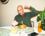 Mann feiert sein **Essen nach Marathon** mit einem kräftigen Bizeps-Zeigen und einem Bissen vom Teller.
