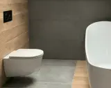 Salle de bain moderne avec un élégant **pose wc suspendu** sur un mur en bois, face à une baignoire blanche et des murs gris.