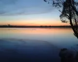 Zachód słońca nad jeziorem, z sylwetką elektrowni w oddali. Na wodzie widać kilka kaczek. To piękny widok, jak z **pogoria 3**.