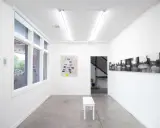 Inside the Atlanta Center for Photography, a white bench sits before a map artwork. Black and white photos line the opposite wall.