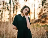 Młoda kobieta w czarnej sukience pozuje na tle zachodzącego słońca i trzcin. Idealna modelka do nauki kurs fotografii portretowej.