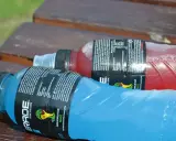 Zimne napoje izotoniczne w butelkach, niebieski i czerwony, leżą na drewnianej ławce. Idealne, by sprawdzić, was hydriert am besten.