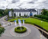 Nowoczesny budynek WSB Gdańsk otoczony zielenią. Na rondzie powiewają białe flagi z logo uczelni.