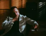 Louis Villain, wiek nieznany, w białej marynarce, zamyślony, siedzi przy biurku.