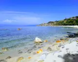 Spiaggia di Tropea con la torre Sant'Irene in lontananza, mare cristallino e rocce sulla riva.