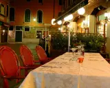 Table dressée devant la trattoria "da Roberto" à Venise, avec des chaises rouges et des verres à vin.