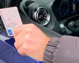 Mano sujetando permiso de conducir español dentro de un coche moderno, anticipando la conducción autónoma en España.
