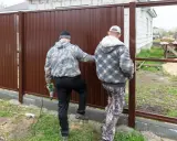 Dwóch mężczyzn montuje brązowy płot. Jeden z nich trzyma wiertarkę. Czy można postawić płot przy płocie?