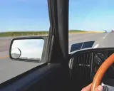 Widok z wnętrza samochodu jadącego po pustej drodze. Kierownica, deska rozdzielcza i lusterko boczne. Pomyśl o tym, jak odzyskać zabrane prawo jazdy za alkohol na 3 lata.