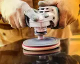 Manos enguantadas usan una pulidora para limpiar piedras, revelando su brillo natural.