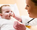 Lekarz bada gardło niemowlaka, sprawdzając jego rozwój. To ważny skok rozwojowy 14 miesiąca.