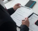 Biznesmen wypełnia formularz, szukając danych NIP, REGON. Na biurku leży też smartfon i notatnik.
