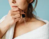 Une femme applique un sérum à base de peptide sur sa peau, enveloppée dans un peignoir blanc douillet.