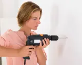 Mujer usando un taladro, mostrando sus partes como el gatillo y la broca, para hacer un agujero en la pared.