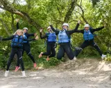 Cinco personas, incluyendo niños, saltan alegres con trajes de neopreno y chalecos salvavidas en un entorno natural, listos para una aventura en Huesca.