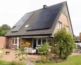 Tak på ett tegelhus med solceller som ger hög verkningsgrad. Solrosor blommar på uteplatsen.