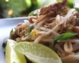 Délicieux pad thai porc avec pousses de soja, cacahuètes et quartiers de citron vert.