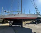 Un voilier blanc et rouge, prêt pour l'aventure, est exposé sur des bers. Ce navire, un modèle de **Gibert Marine**, attend de retrouver les flots.