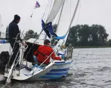 Deux hommes naviguent sur un voilier micro challenger, le vent gonflant les voiles sur un lac calme.