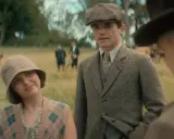Giovane donna con cappello a scacchi e gilet a rombi, accanto a un uomo con berretto e giacca di tweed. Sullo sfondo, i sette quadranti di un campo.